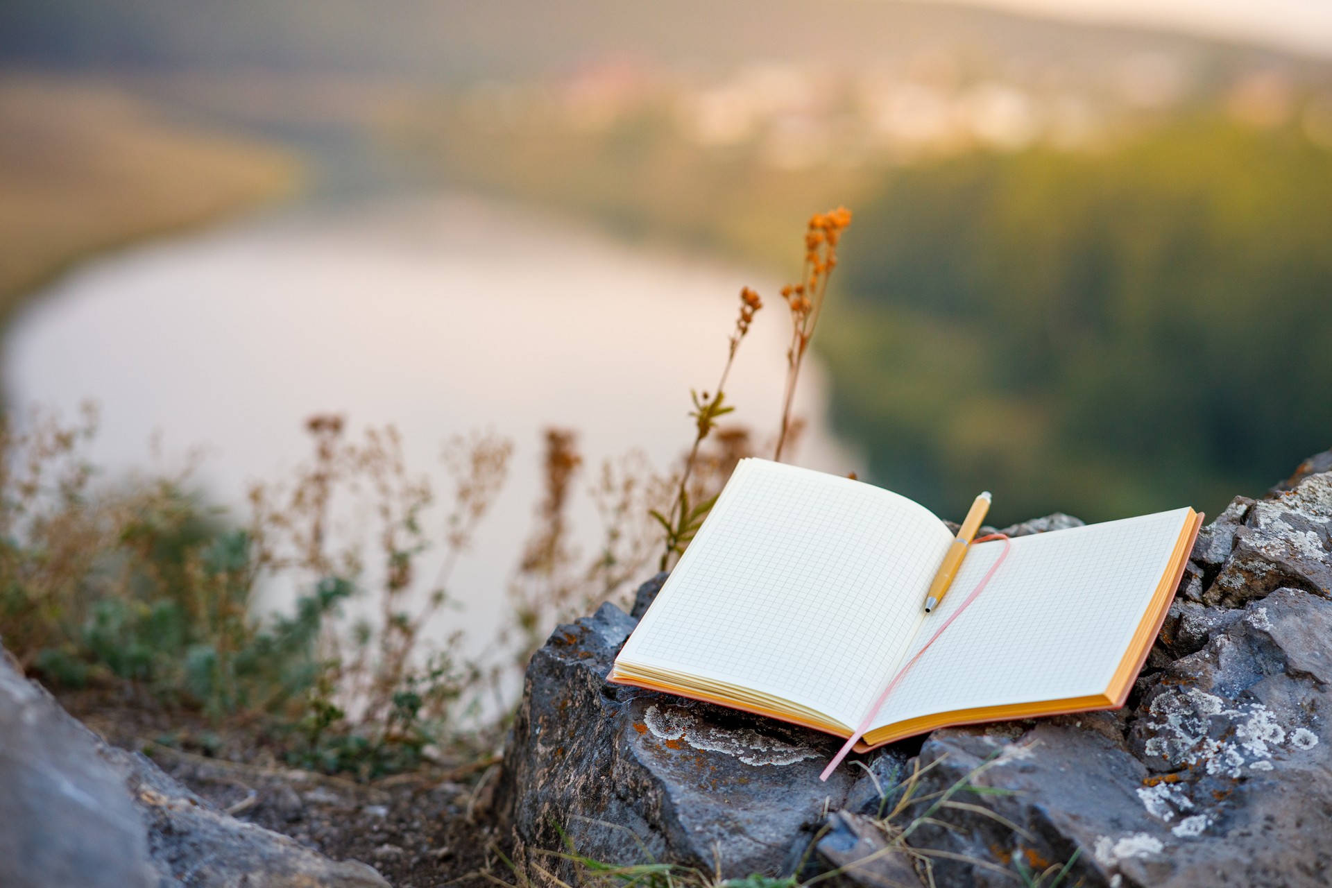 an open empty book with a fountain pen outdoors, the background is a blurred river and forest